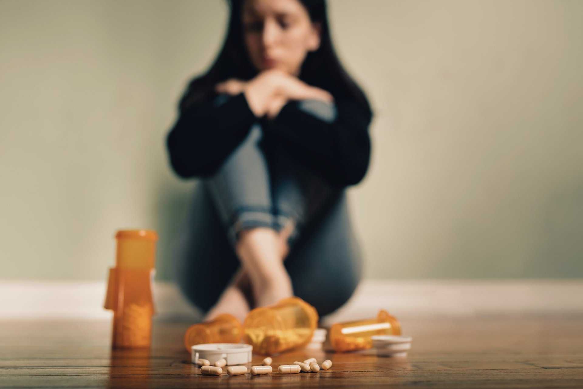 woman sitting by the wall looking at a bottle of with pills coming out