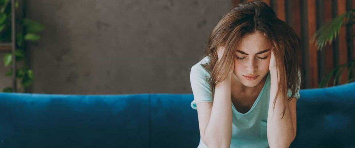a women sits on a blue couch with her head in her hands struggling with addiction
