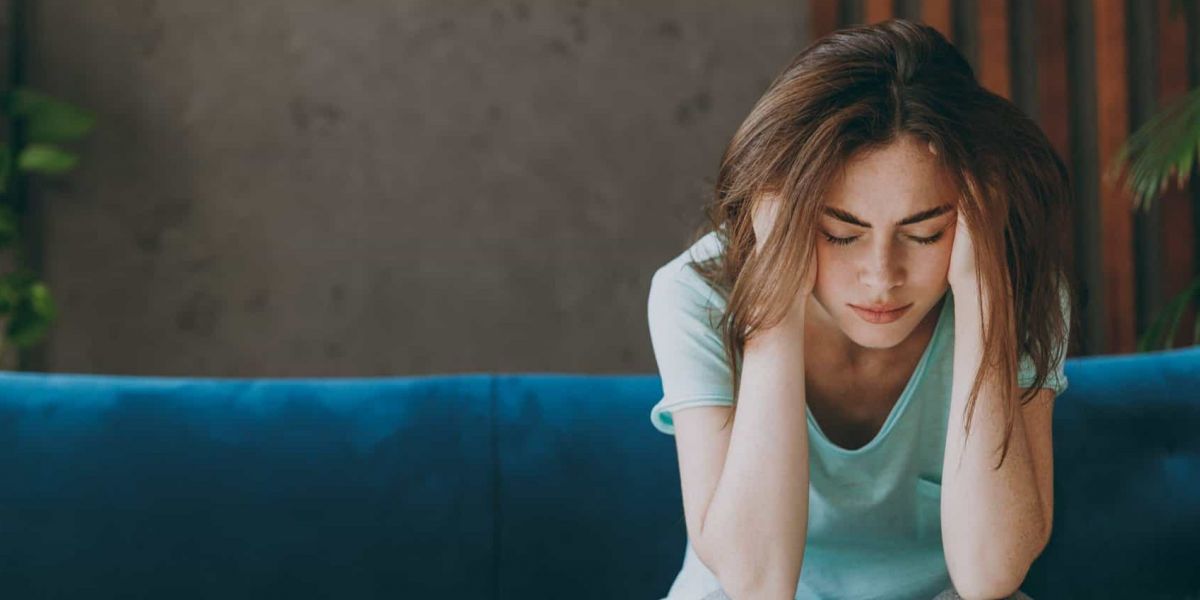 a women sits on a blue couch with her head in her hands struggling with addiction