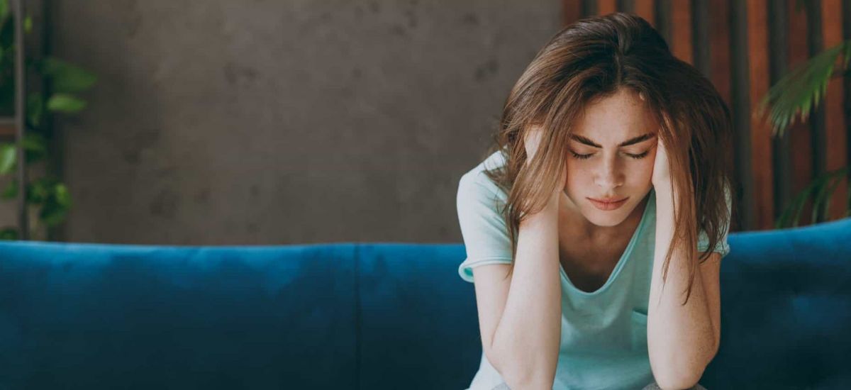 a women sits on a blue couch with her head in her hands struggling with addiction