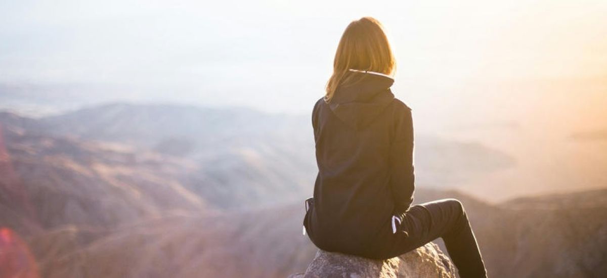 young girl sits on the ledge of a cliff looking off into the distance