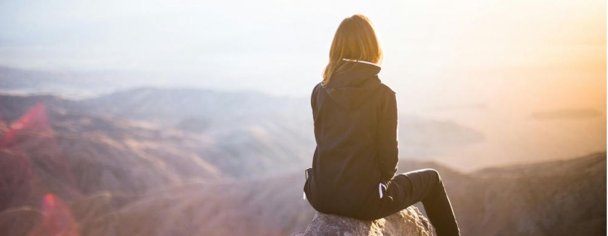 young girl sits on the ledge of a cliff looking off into the distance