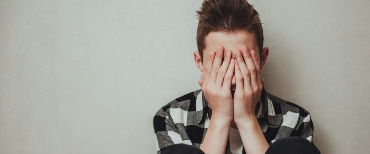 young man sitting on the ground with his head in his hands as he struggled with substance abuse