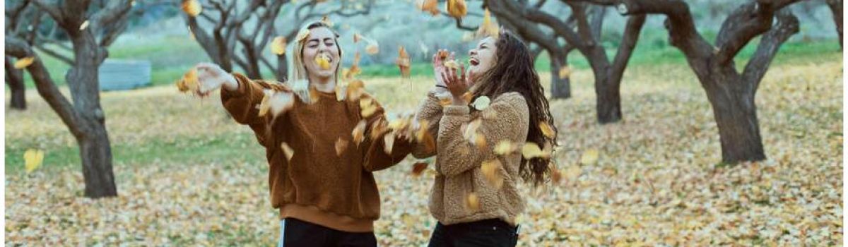 two girls happily throwing falling leaves up in the air
