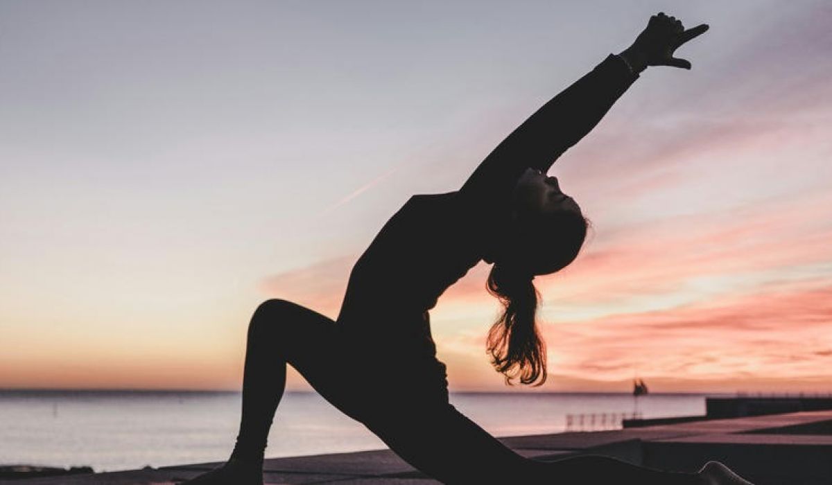 a woman doing a yoga pose behind a sunset