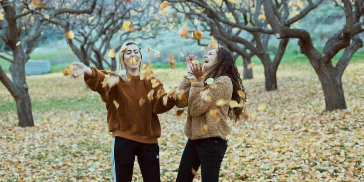 two girls happily throwing falling leaves up in the air