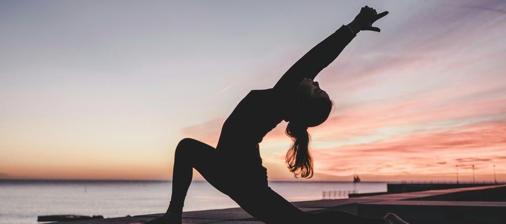 a woman doing a yoga pose behind a sunset
