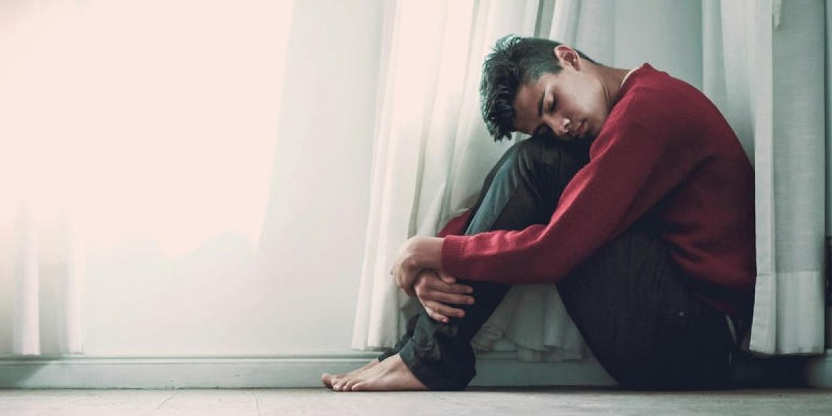 young man is sitting on the floor with his head in his knees struggling with mental health issues